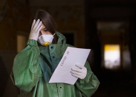 girl medic in a mask and a protective suit stands in the clinic with documentsの写真素材