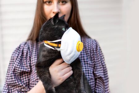 Girl Holding Cat in Hands. Cat wearing medical mask because of Coronavirus or air pollution or virus epidemic in the city. Place for text, Copy space. The concept of COVID-19 virus.の写真素材