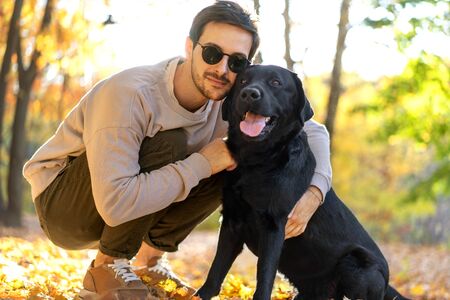 guy in sunglasses hugs his dog in autumn parkの写真素材