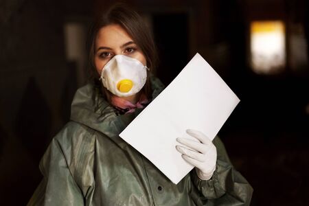 a girl medic in a mask and a protective suit is standing in the clinic with documents about the coronavirusの写真素材
