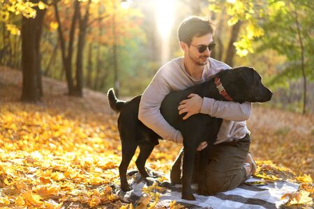 guy in sunglasses hugs his dog in autumn parkの写真素材