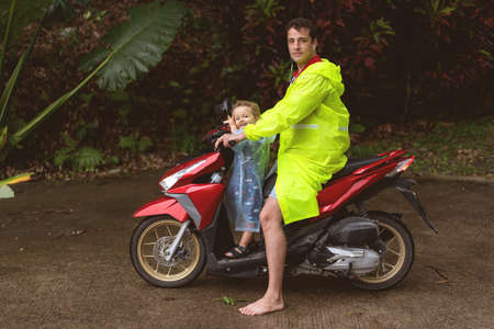 dad with his son on a moped in a tropical growth among palm treesの写真素材
