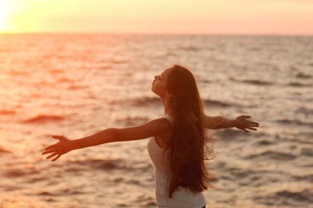Free woman enjoying freedom feeling happy at beach at sunset. Beautiful serene relaxing woman in pure happiness and elated enjoyment with arms raised outstretched up. Asian Caucasian female model.の写真素材