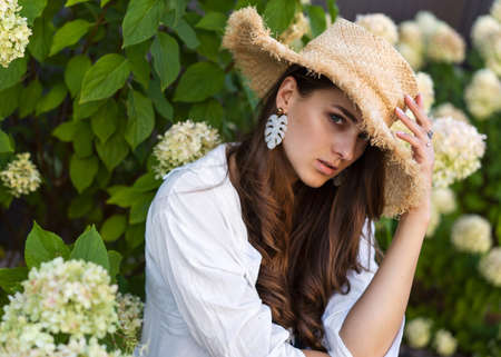 beautiful fashion girl posing on the background of hydrangeas in a straw hat and rays of lightの写真素材