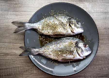 raw dorado fish on a plate sprinkled with spices before cooking by the chefの写真素材