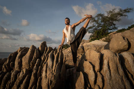 guy doing yoga poses on sharp rocks near the beach in Thailandの写真素材
