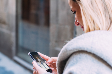Young beautiful blond woman touching and browsing her smart phone over city backgroundの写真素材