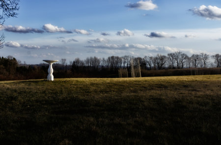 A white sculpture in a field with trees and clouds in the backgroundの写真素材