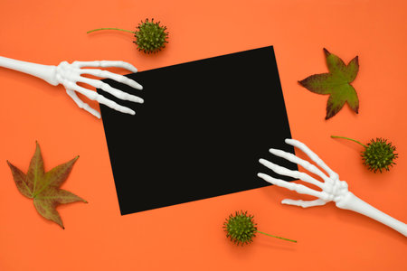 Halloween skeleton hands with maple leaves on orangeの写真素材