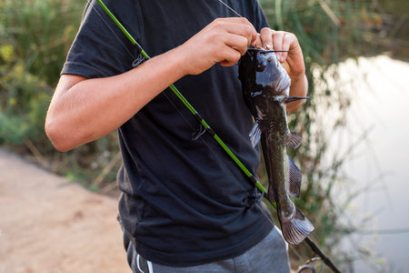Young fisherman taking a fish off the hookの写真素材