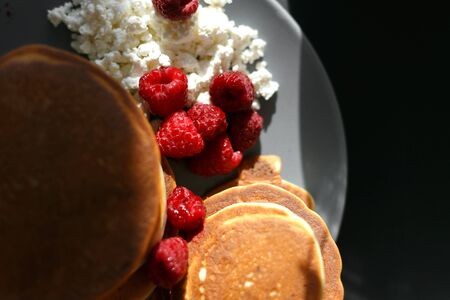 Pancakes with cottage cheese and raspberries on a gray plate, on a black backgroundの写真素材