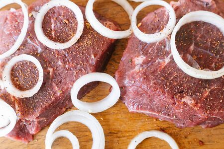 Raw beef meat with onion rings and spices on a wooden backgroundの写真素材