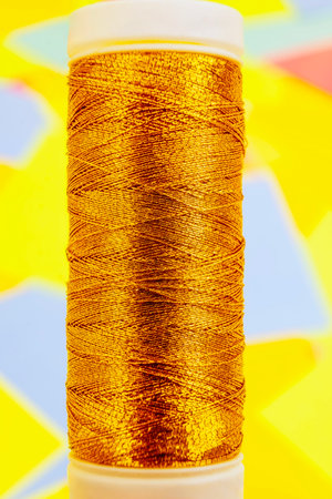 One twisted cylindrical new clean bobbin full of golden synthetic threadsの写真素材