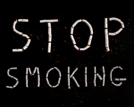 Text stop smoking made from broken cigarettes with faces painted on black backgroundの写真素材