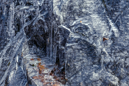 Narrow streams of water run under a thin sheet of ice and over stone