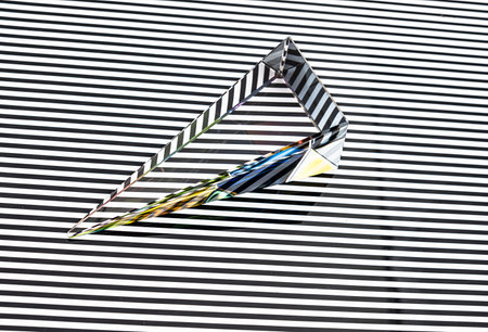 Glass pyramid prism with colorful light reflection on white horizontal stripe on black backgroundの写真素材
