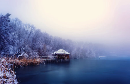 wooden pier for fishing with a roof of straw on a frozen lake on a foggy winter dayの写真素材