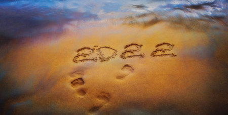 2022 is drawing on yellow sand on a beach with a wave by the sea