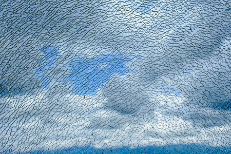 Blue cloudy sky behind the cracked glass