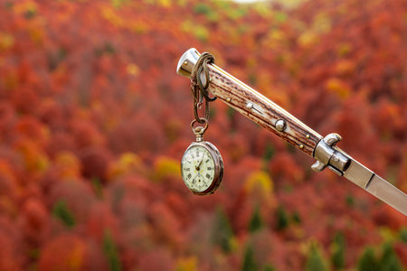 an old watch hanging from a knife with an autumn landscape in the backgroundの写真素材