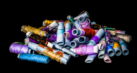 Pile of used colorful spools of thread tailoring, on black background
