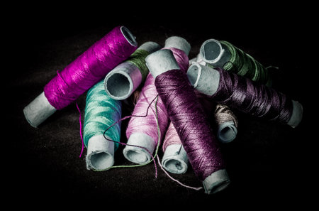 Pile of used colorful spools of thread tailoring, on black backgroundの写真素材