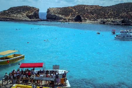 Comino, Malta - July 18, 2019. Tourists crowd at Blue Lagoon to enjoy the clear turquoise water on a sunny summer day with and boats on Comino island, Malta.のeditorial素材