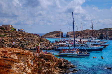 Comino, Malta - July 18, 2019. Tourists crowd at Blue Lagoon to enjoy the clear turquoise water on a sunny summer day with and boats on Comino island, Malta.のeditorial素材