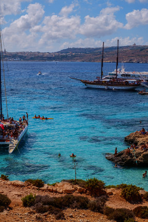 Comino, Malta - July 18, 2019. Tourists crowd at Blue Lagoon to enjoy the clear turquoise water on a sunny summer day with and boats on Comino island, Malta.のeditorial素材