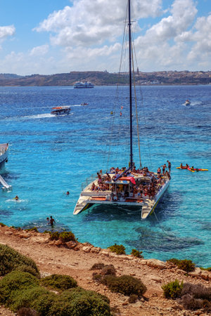 Comino, Malta - July 18, 2019. Tourists crowd at Blue Lagoon to enjoy the clear turquoise water on a sunny summer day with and boats on Comino island, Malta.のeditorial素材