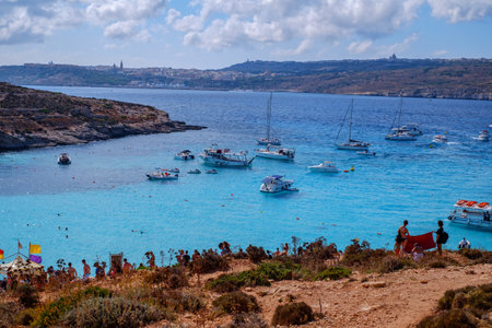 Comino, Malta - July 18, 2019. Tourists crowd at Blue Lagoon to enjoy the clear turquoise water on a sunny summer day with and boats on Comino island, Malta.のeditorial素材
