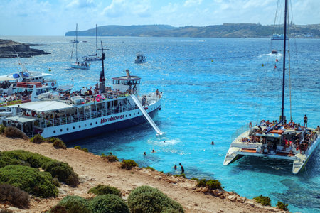 Comino, Malta - July 18, 2019. Tourists crowd at Blue Lagoon to enjoy the clear turquoise water on a sunny summer day with and boats on Comino island, Malta.のeditorial素材