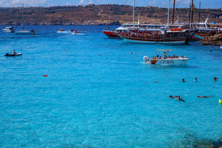 Comino, Malta - July 18, 2019. Tourists crowd at Blue Lagoon to enjoy the clear turquoise water on a sunny summer day with and boats on Comino island, Malta.のeditorial素材
