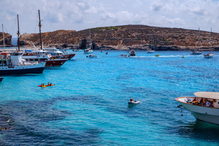 Comino, Malta - July 18, 2019. Tourists crowd at Blue Lagoon to enjoy the clear turquoise water on a sunny summer day with and boats on Comino island, Malta.のeditorial素材