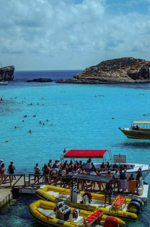 Comino, Malta - July 18, 2019. Tourists crowd at Blue Lagoon to enjoy the clear turquoise water on a sunny summer day with and boats on Comino island, Malta.のeditorial素材