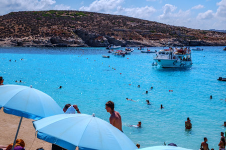 Comino, Malta - July 18, 2019. Tourists crowd at Blue Lagoon to enjoy the clear turquoise water on a sunny summer day with and boats on Comino island, Malta.のeditorial素材