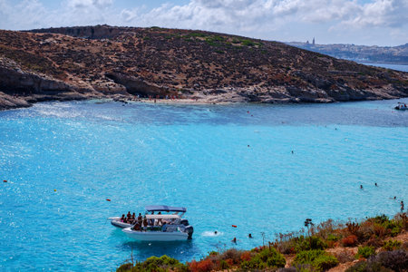 Comino, Malta - July 18, 2019. Tourists crowd at Blue Lagoon to enjoy the clear turquoise water on a sunny summer day with and boats on Comino island, Malta.のeditorial素材