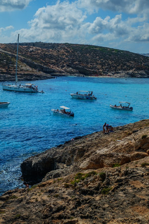 Comino, Malta - July 18, 2019. Tourists crowd at Blue Lagoon to enjoy the clear turquoise water on a sunny summer day with and boats on Comino island, Malta.のeditorial素材