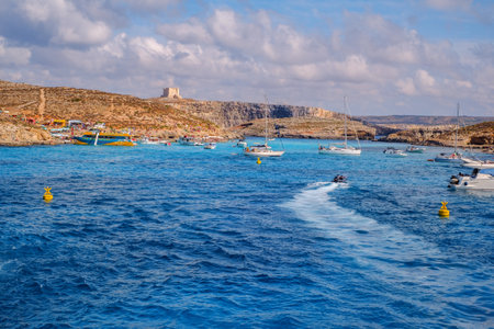 Comino, Malta - July 18, 2019. Tourists crowd at Blue Lagoon to enjoy the clear turquoise water on a sunny summer day with and boats on Comino island, Malta.のeditorial素材