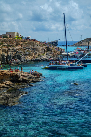 Comino, Malta - July 18, 2019. Tourists crowd at Blue Lagoon to enjoy the clear turquoise water on a sunny summer day with and boats on Comino island, Malta.のeditorial素材