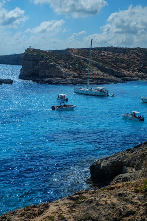 Comino, Malta - July 18, 2019. Tourists crowd at Blue Lagoon to enjoy the clear turquoise water on a sunny summer day with and boats on Comino island, Malta.のeditorial素材