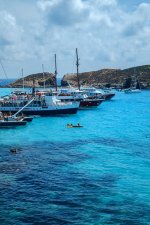 Comino, Malta - July 18, 2019. Tourists crowd at Blue Lagoon to enjoy the clear turquoise water on a sunny summer day with and boats on Comino island, Malta.のeditorial素材