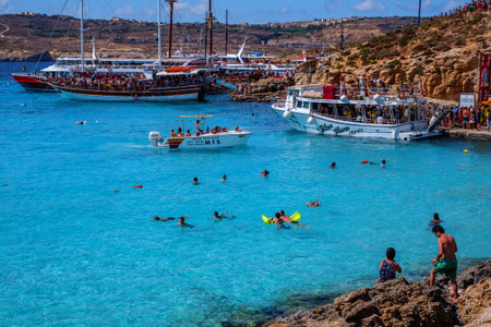 Comino, Malta - July 18, 2019. Tourists crowd at Blue Lagoon to enjoy the clear turquoise water on a sunny summer day with and boats on Comino island, Malta.のeditorial素材