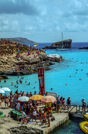 Comino, Malta - July 18, 2019. Tourists crowd at Blue Lagoon to enjoy the clear turquoise water on a sunny summer day with and boats on Comino island, Malta.のeditorial素材