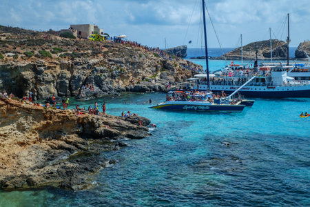 Comino, Malta - July 18, 2019. Tourists crowd at Blue Lagoon to enjoy the clear turquoise water on a sunny summer day with and boats on Comino island, Malta.のeditorial素材