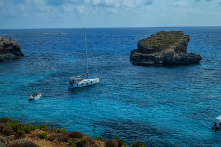 Comino, Malta - July 18, 2019. Tourists crowd at Blue Lagoon to enjoy the clear turquoise water on a sunny summer day with and boats on Comino island, Malta.のeditorial素材