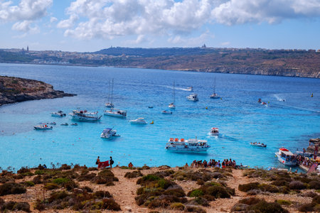 Comino, Malta - July 18, 2019. Tourists crowd at Blue Lagoon to enjoy the clear turquoise water on a sunny summer day with and boats on Comino island, Malta.のeditorial素材