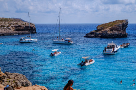 Comino, Malta - July 18, 2019. Tourists crowd at Blue Lagoon to enjoy the clear turquoise water on a sunny summer day with and boats on Comino island, Malta.のeditorial素材