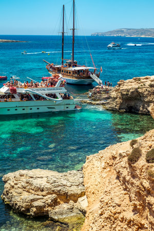 Comino, Malta - July 23, 2019. Tourists crowd at Blue Lagoon to enjoy the clear turquoise water on a sunny summer day with boats on Comino island, Malta.のeditorial素材