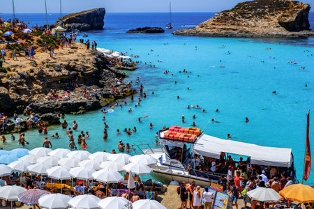 Comino, Malta - July 23, 2019. Tourists crowd at Blue Lagoon to enjoy the clear turquoise water on a sunny summer day with boats on Comino island, Malta.のeditorial素材